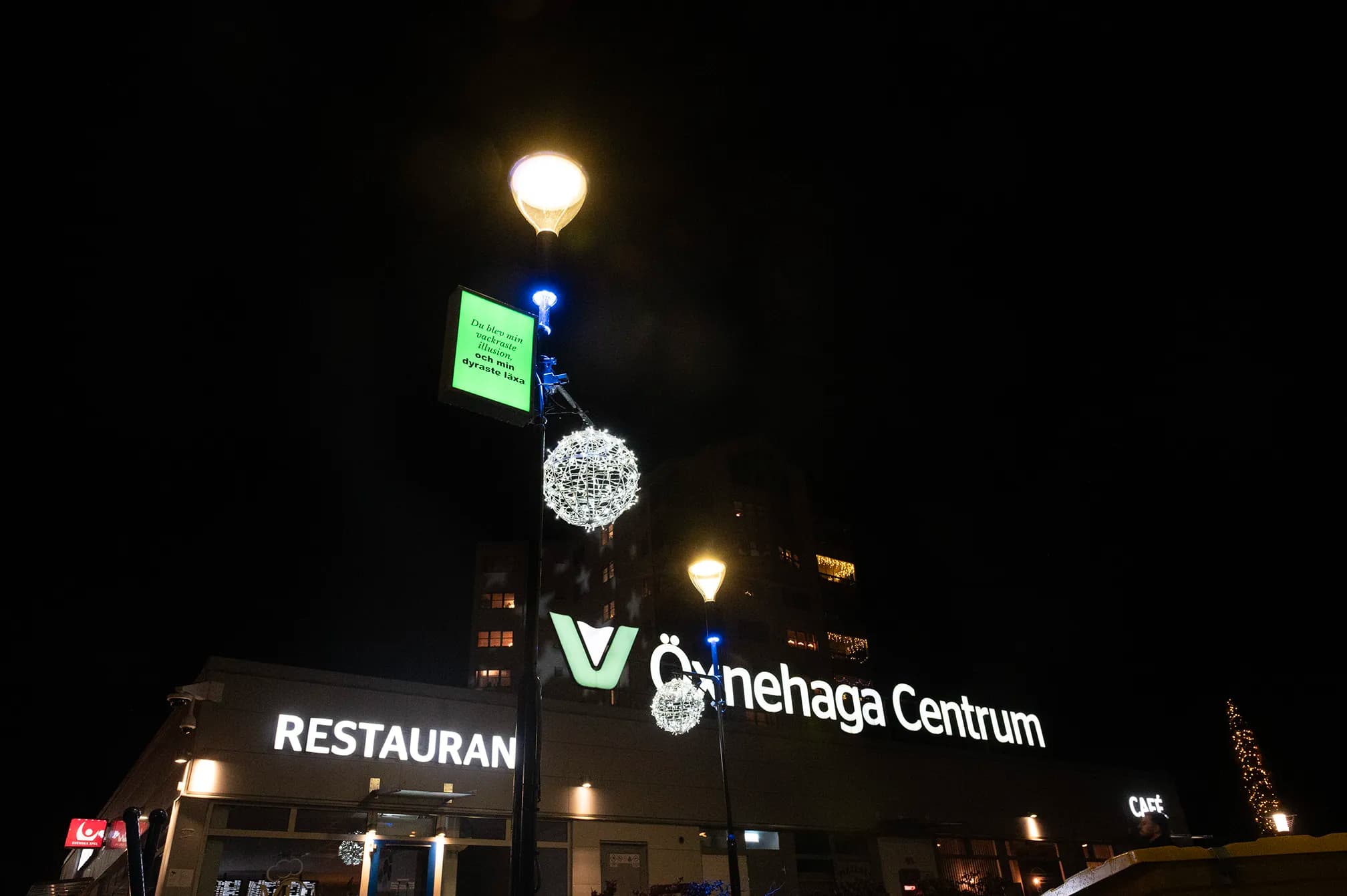 Poesiskylt med belysning uppsatt på en lyktstolpe vid Öxnehaga centrum